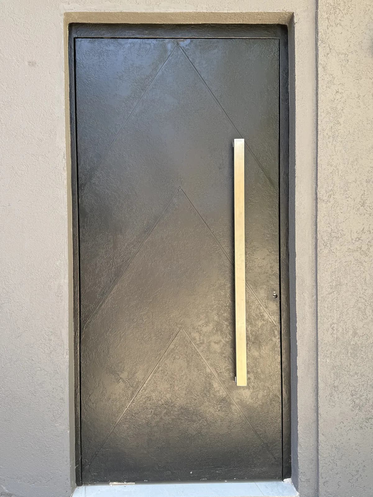 Puerta pivotante de chapa negra con relieve chevron y barral de acero