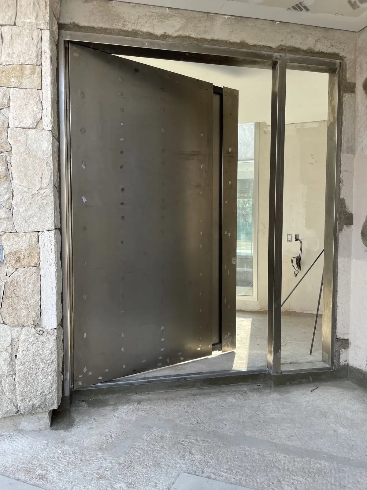 Puerta pivotante de chapa con terminación oxidada, abierta sobre su eje, en obra